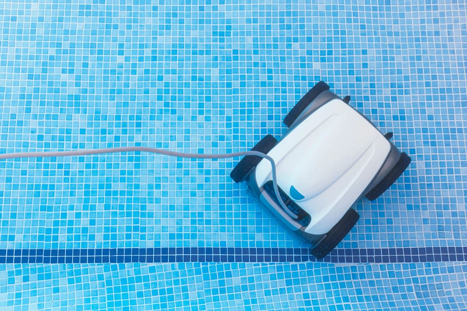 Robot nettoyeur automatique de piscine en fonctionnement sur carrelage mosaïque bleue, câble d'alimentation visible
