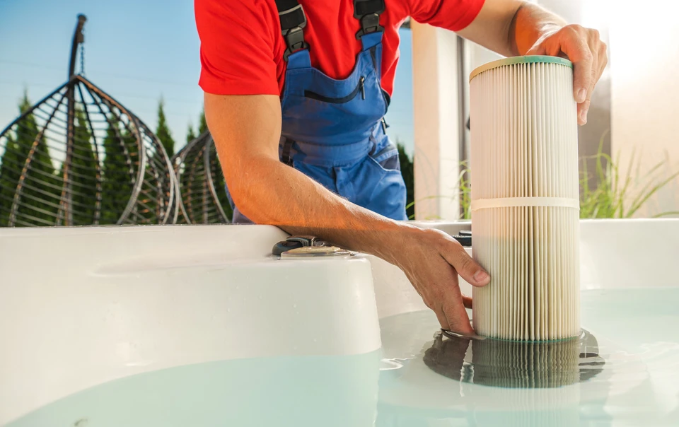 Technicien en combinaison rouge effectuant maintenance sur spa extérieur, agenouillé avec caisse à outils rouge ouverte