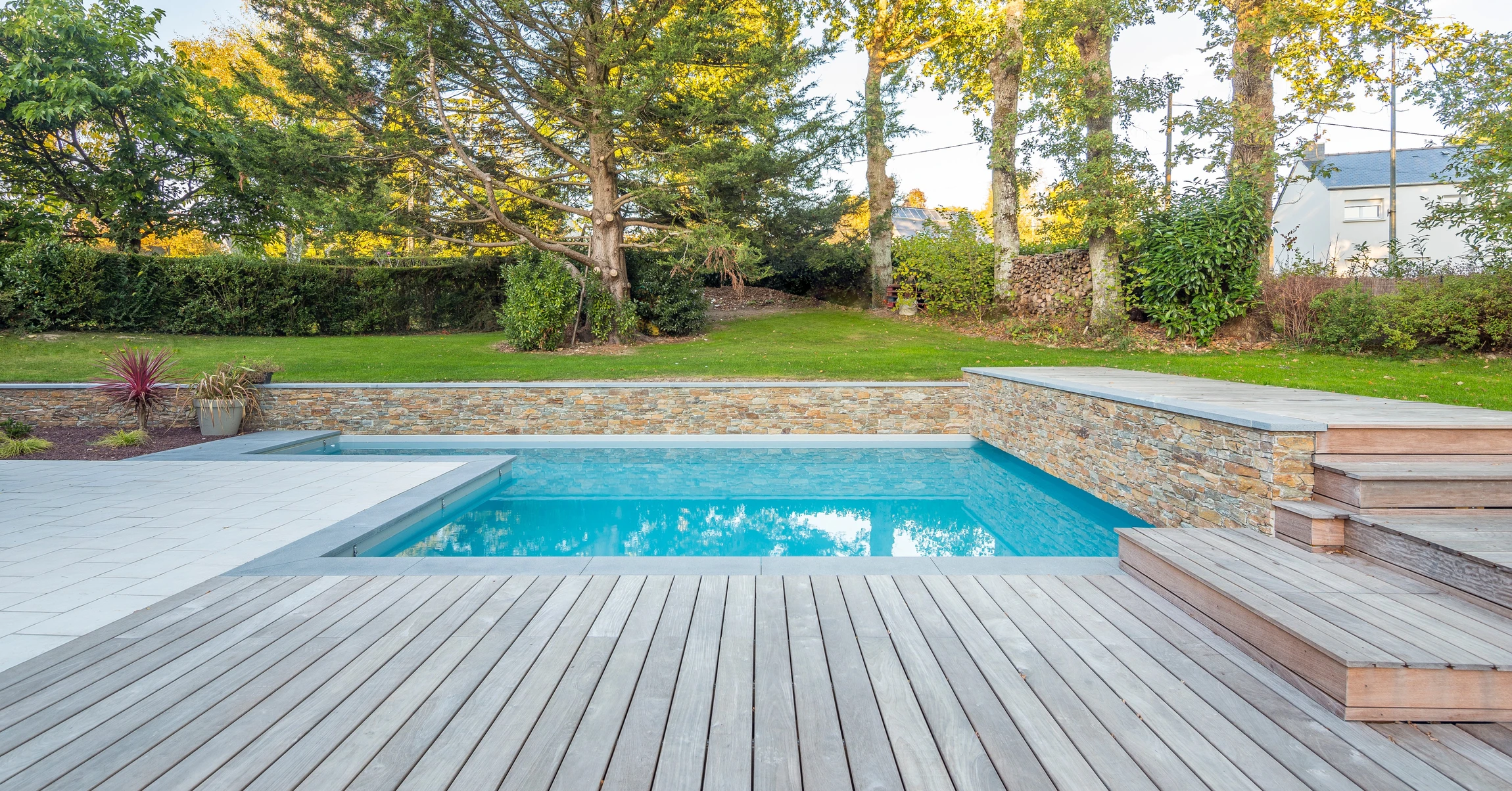 Espace extérieur résidentiel avec piscine rectangulaire à débordement, entourée de dallage en pierre naturelle claire